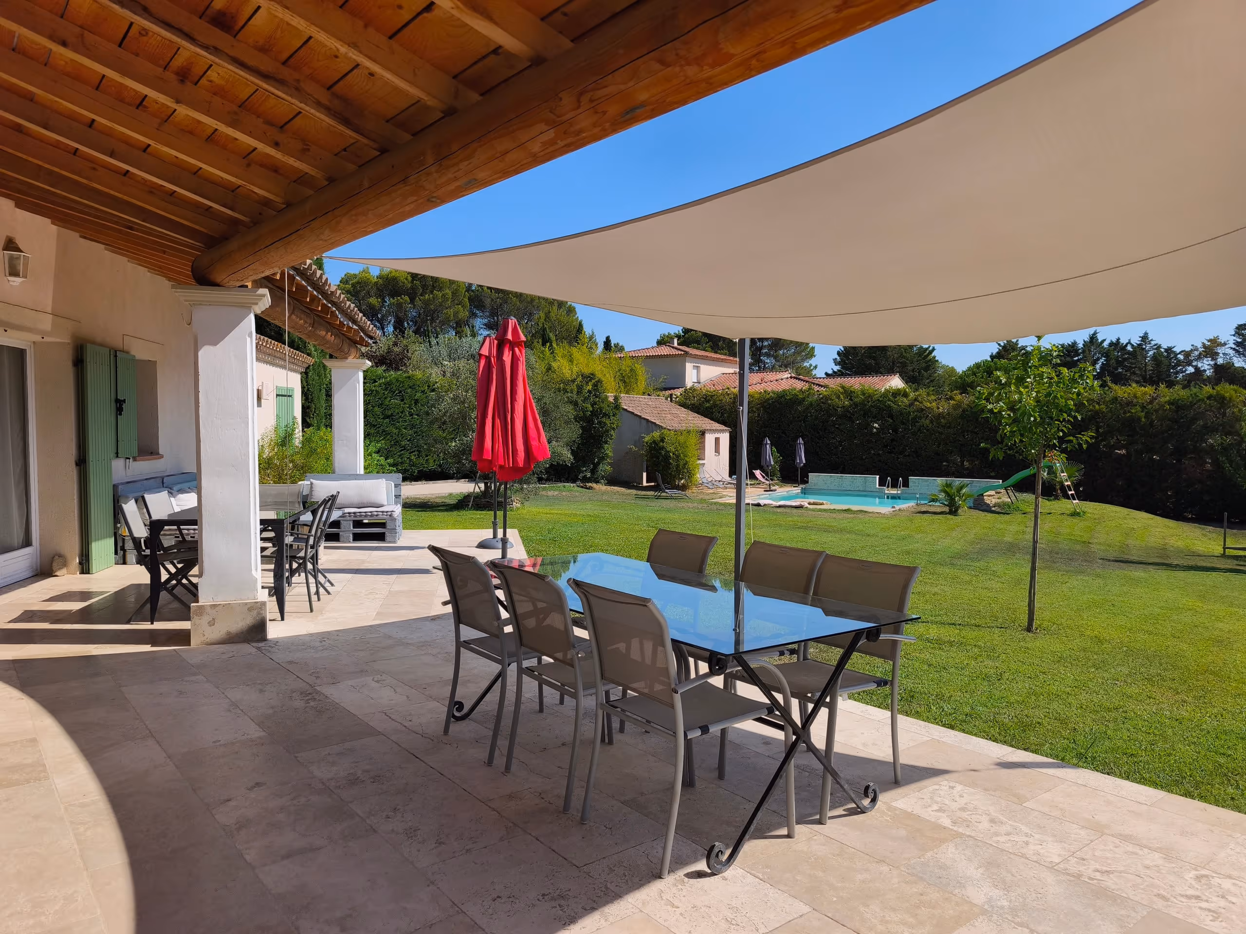 La terrasse couverte de la Villa Roucas, sa table de repas et le jardin en arrière-plan